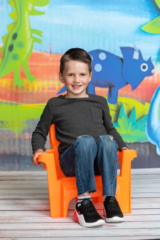 Young boy seated in orange chair for daycare photo day full-length portrait - Meridian Idaho school photographer