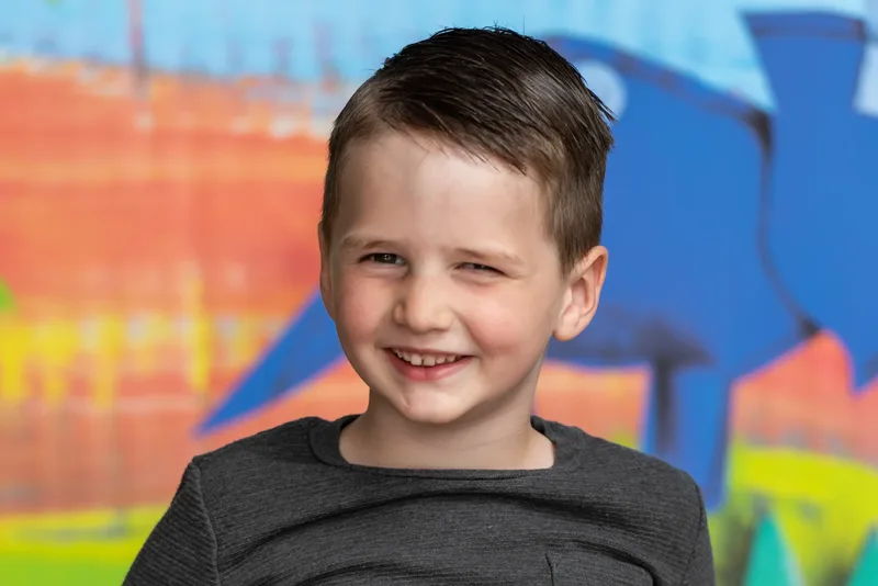 Preschool boy headshot with painted dinosaur backdrop at photo day - daycare photographer Meridian Idaho