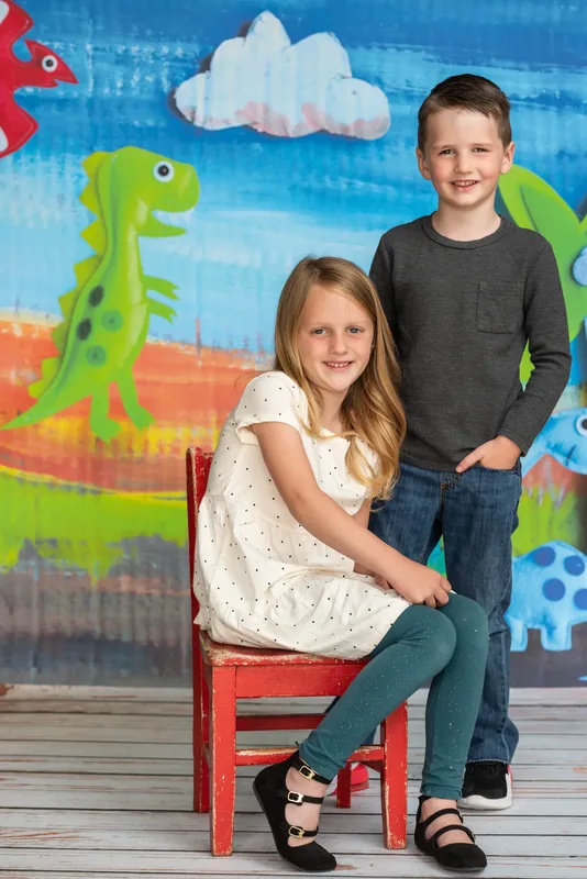 Brother and sister posed together at preschool photo day with colorful dinosaur backdrop - school photography Meridian Idaho