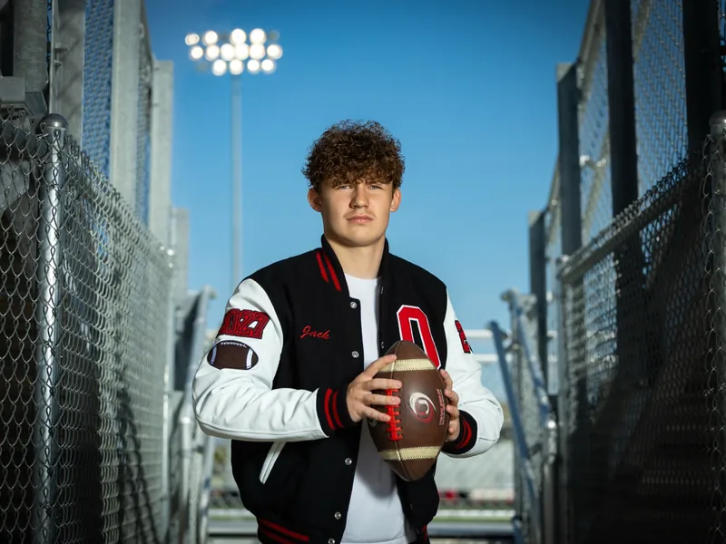 Owyhee High School football senior portrait in a letterman jacket holding a football in the stadium tunnel, Meridian Idaho