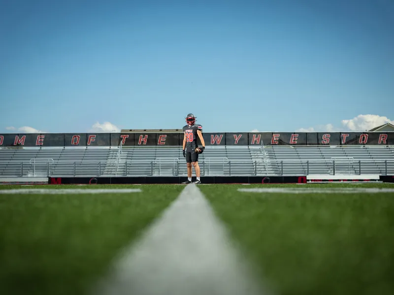 Owyhee Storm football senior in uniform standing on the home field below the Home of the Owyhee Storm sign, Meridian Idaho